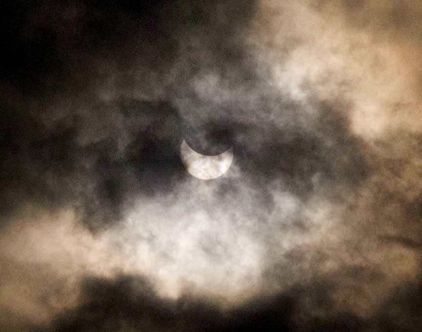 partially eclipse sun peeks through clouds